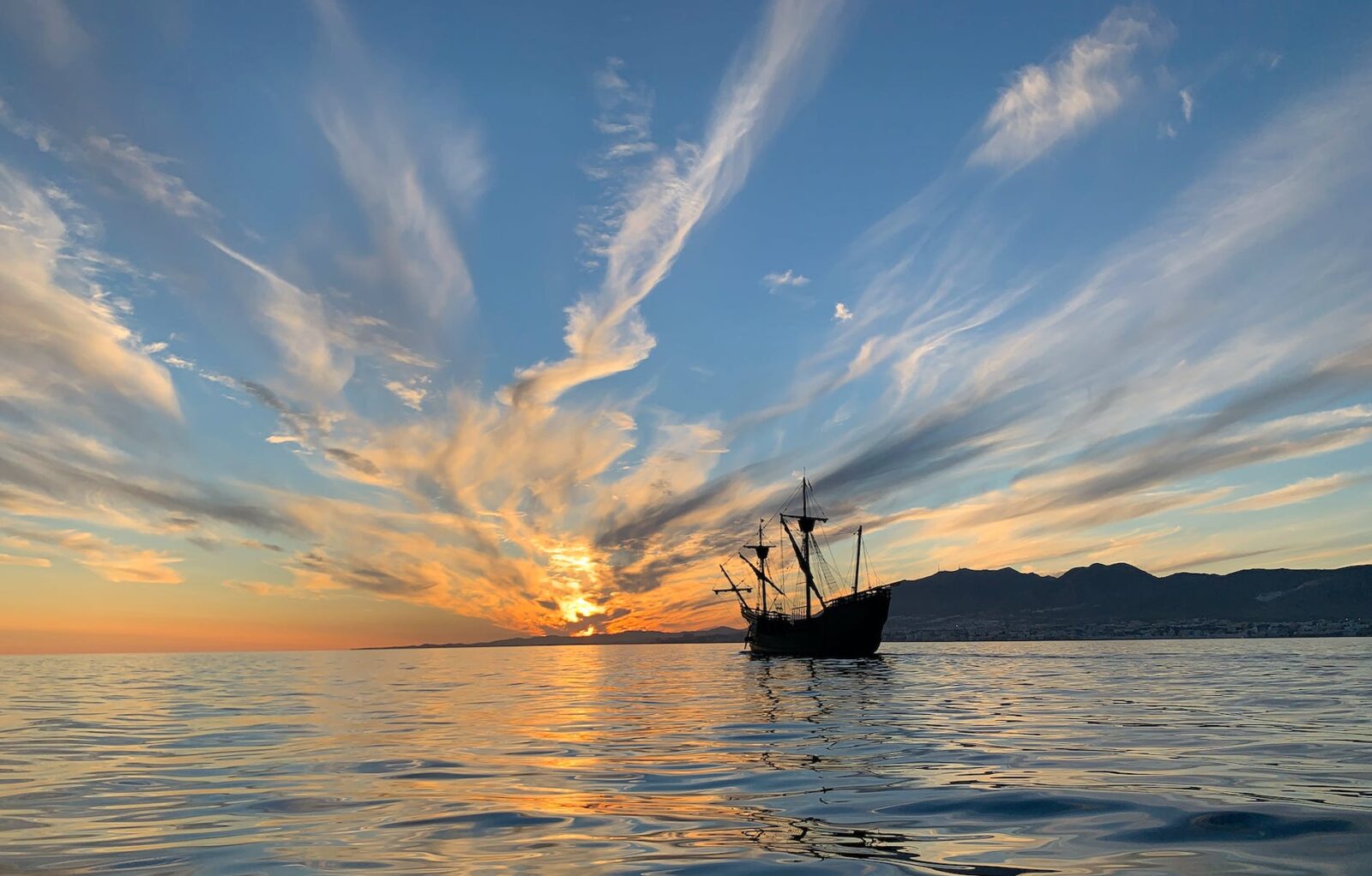 silhouette of a pirate ship sailing on sea during golden hour