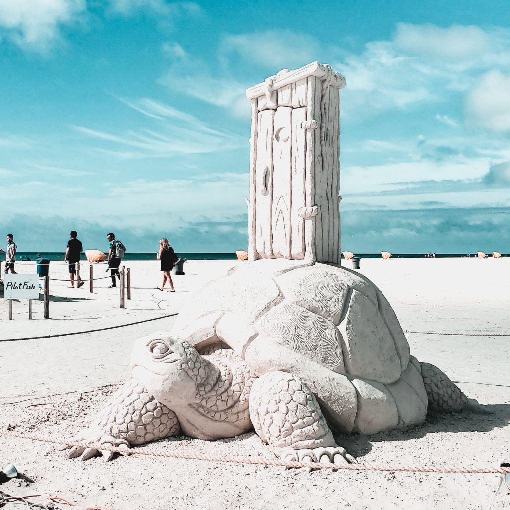 Sand sculpture of a turtle with an out house on the beach in treasure island