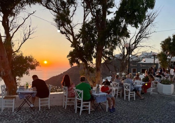 people sitting along cliffside of santorini at sunset