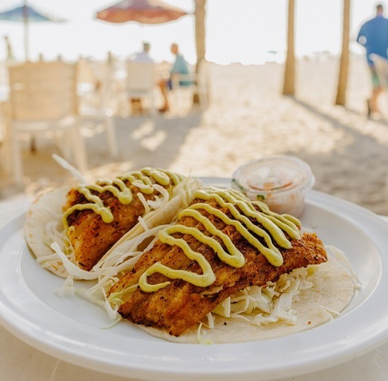 fish tacos drizzled with yellow sauce on the beach
