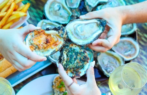 three people holding oysters with fries in the background