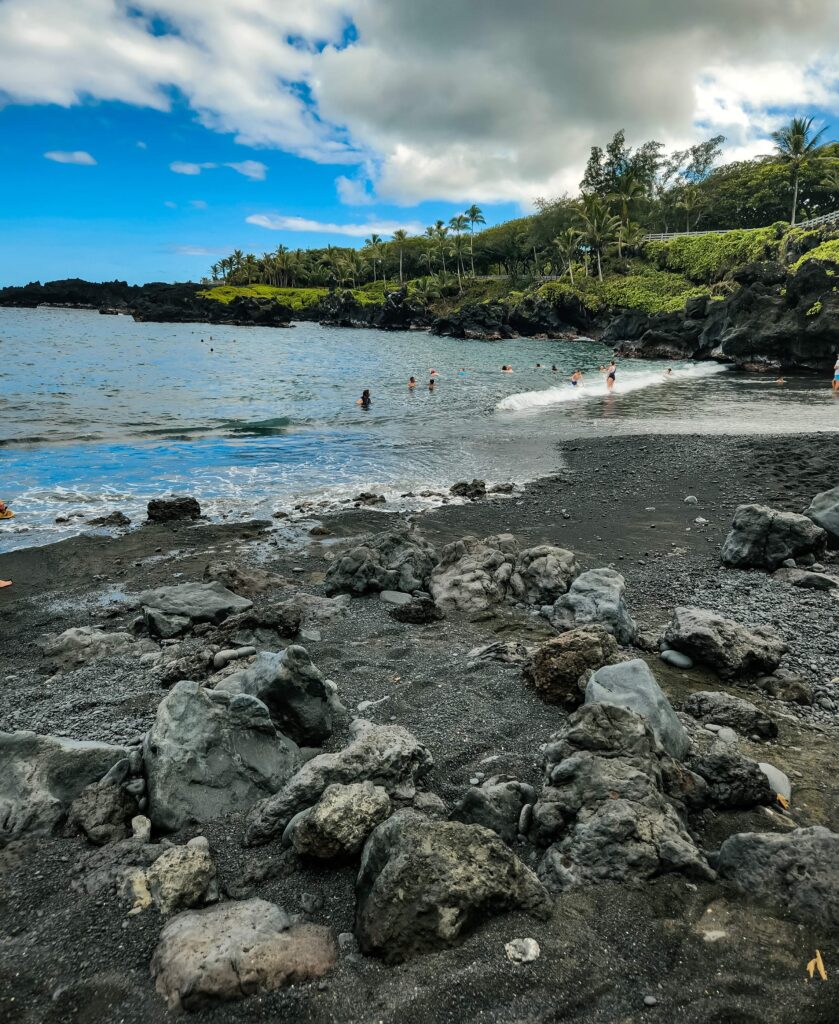 black sand beach inside waianapanapa state park with large rocks