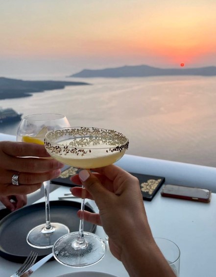 two women with champagne at table with a view of a sunset in fira santorini