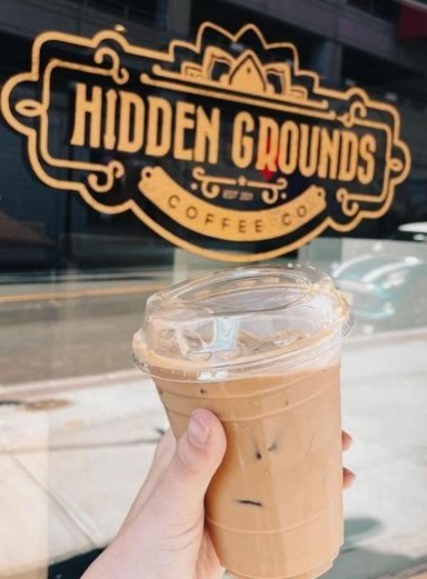 holding iced coffee in front of hidden grounds logo in new jersey