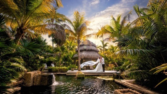 a married couple standing near water with palm trees