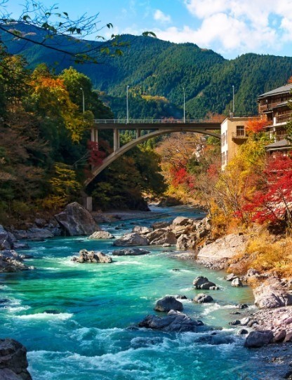 long bridge suspended over blue water with green mountains in japan