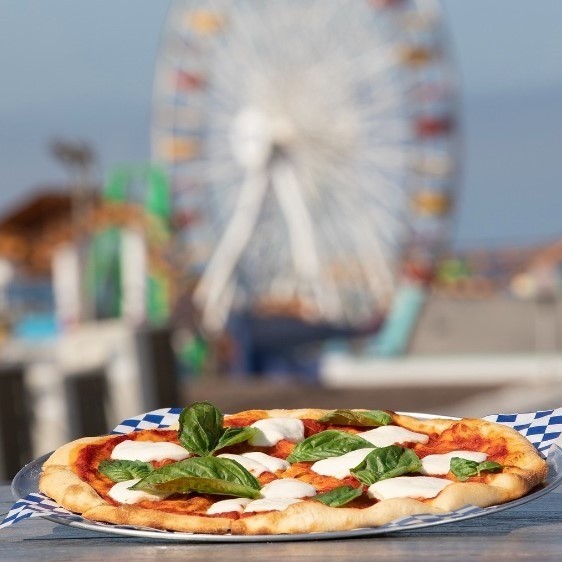 cheese and veggie pizza with a background of the santa monica pier