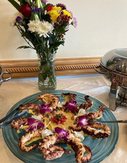 grilled octopus on a blue plate with flowers in a vase