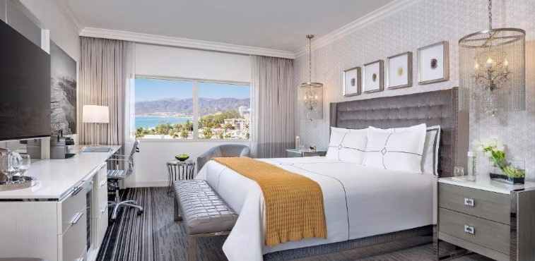a large bed with two bedside light fixtures and a grey headboard with a view of santa monica.