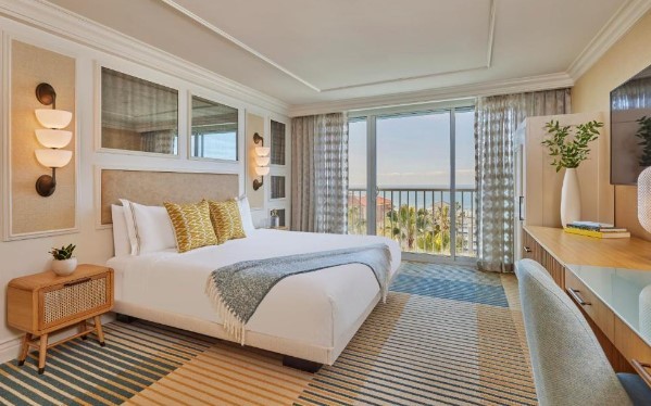 a large bed with yellow pillows and striped carpet with a view of the ocean in santa monica boutique hotel